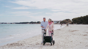 Elderly couple walking on the beach with a walker