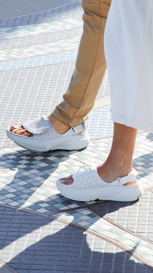 Man wearing gray sandals walking alongside a woman wearing white sandals